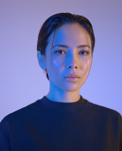 Portr&auml;tt av kvinna med kort h&aring;r, kl&auml;dd i svart tr&ouml;ja, belyst av bl&aring;tt ljus, uttrycker professionalitet och stil.