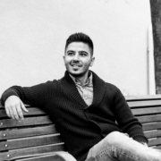 Man som sitter p&aring; en b&auml;nk, kl&auml;dd i en svart kofta och jeans, leende mot kameran, representerar Enkelwebb-teamets personliga och professionella service.