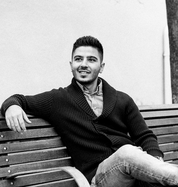 Mikael M. sittande p&aring; en b&auml;nk, leende, if&ouml;rd en svart kofta och skjorta, representerar grundaren och VD:n av Enkelwebb med fokus p&aring; webbl&ouml;sningar och anv&auml;ndarv&auml;nlig design.