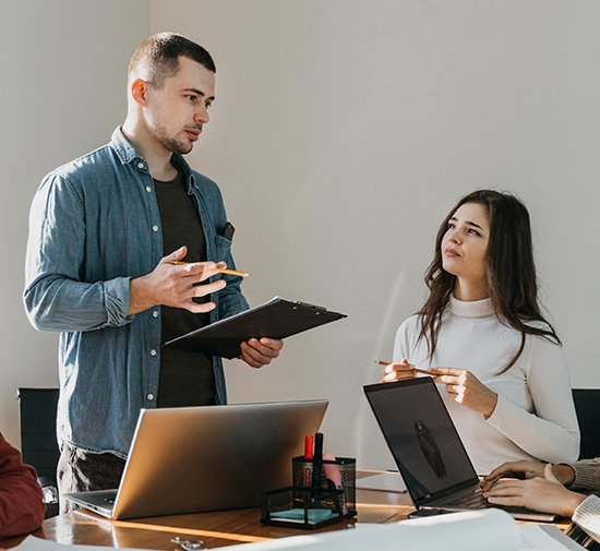 M&ouml;te mellan kollegor med b&auml;rbara datorer, man med anteckningsblock och kvinna som lyssnar, illustrerar samarbete inom webbdesign.
